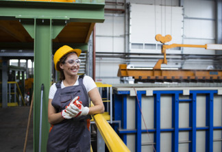 Portrait of smiling female factory worker standing in industrial production hall.