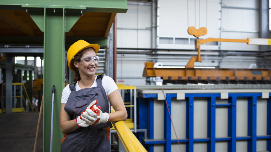 Portrait of smiling female factory worker standing in industrial production hall.